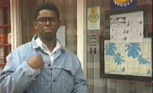 Image of Kevin Buckle. Kevin is a young Black man wearing a denim jacket and thick rimmed glasses. 