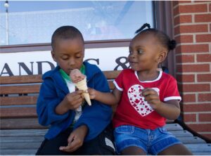 Two Black children sharing ice cream on a bench