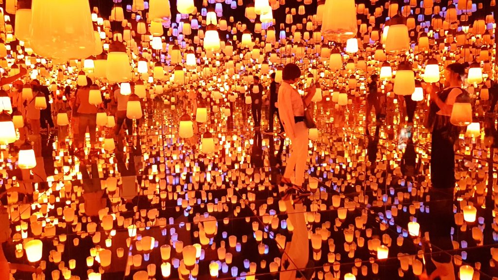 a mass of hanging orange lanterns reflected below by a mirror floor