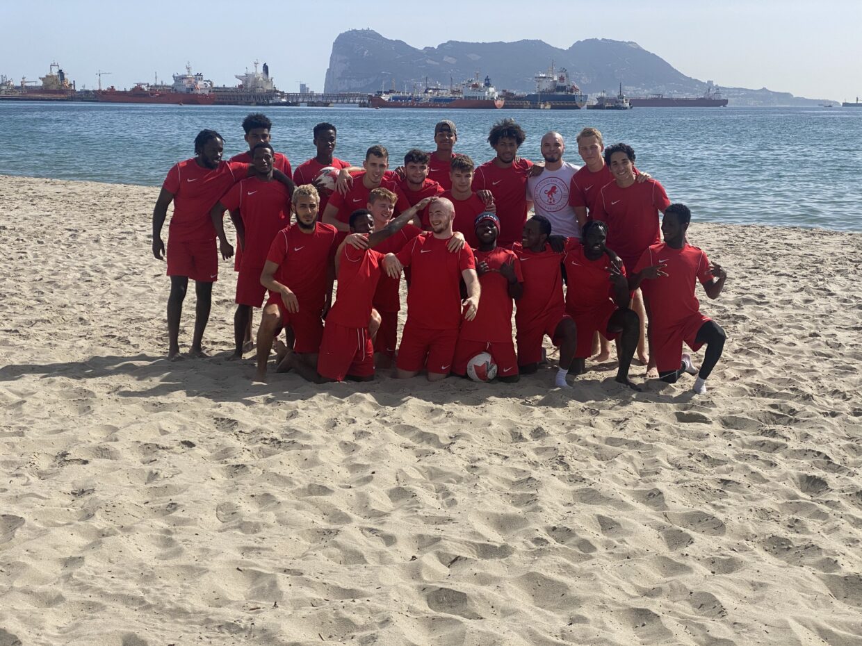 Group photo of the Atletico san Jorge team wearing red shirts and shorts stood on a beach.