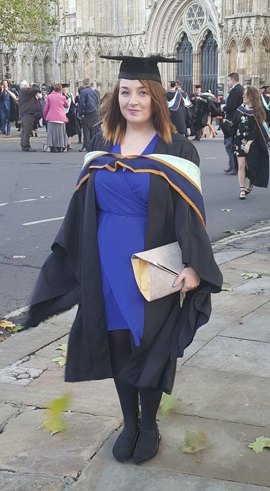 Hannah is standing outside of York Minster on her graduation. Hannah is wearing a graduation gown, motorboard and a blue dress.