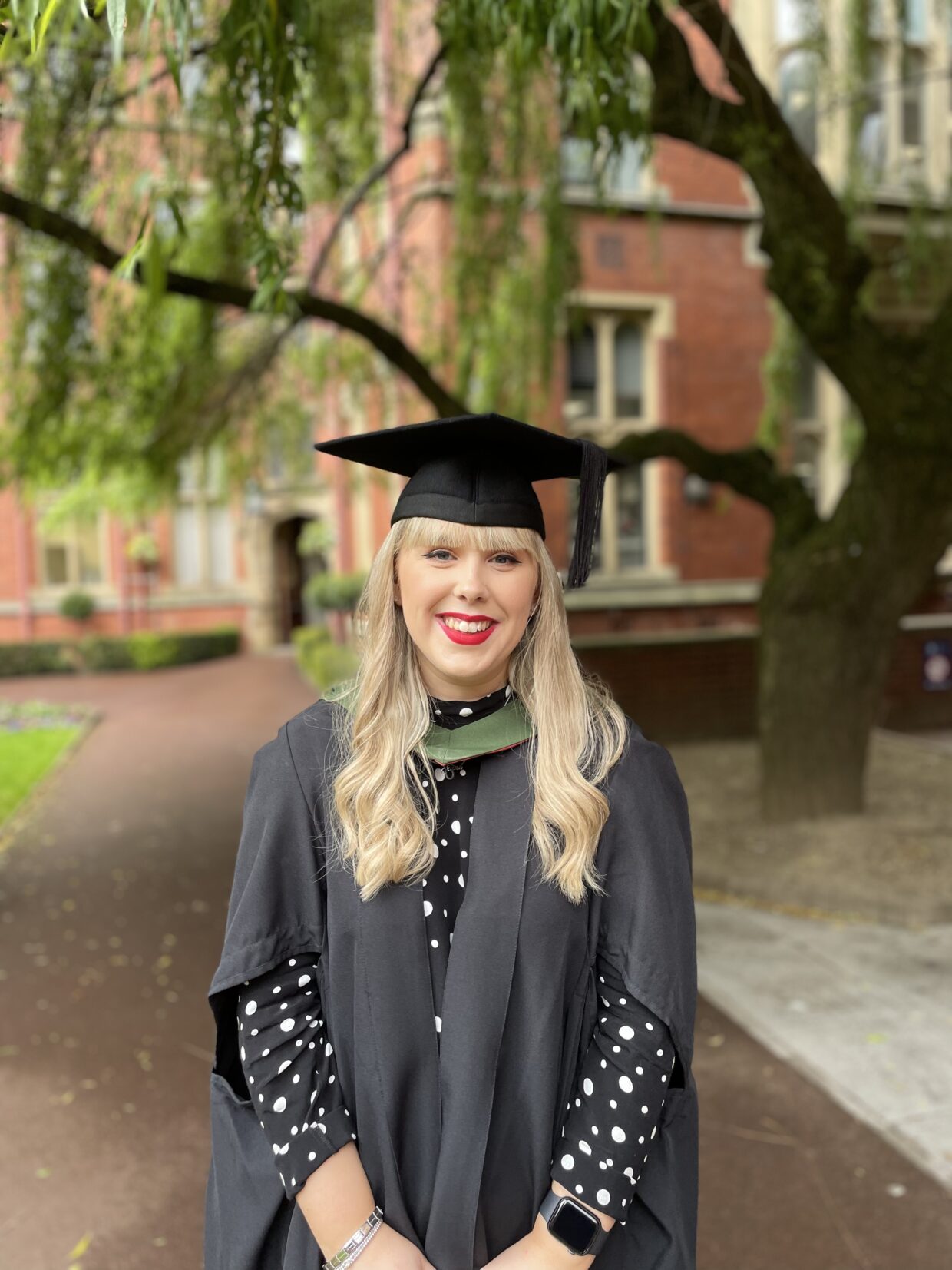 Jenna has long blonde hair and is smiling at the camera. She is wearing a graduation cap and gown during her Master's graduation at the University of Sheffield