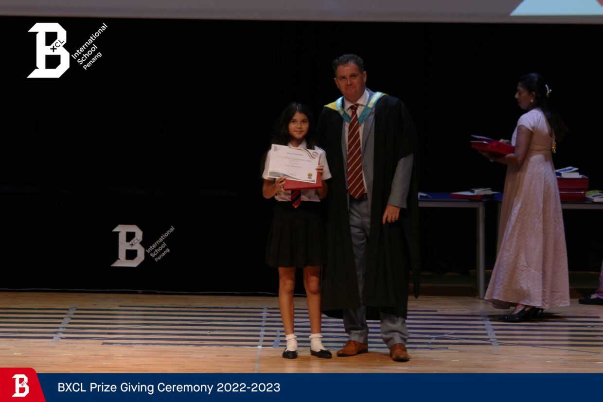 Duncan is stood on stage with his youngest daughter awarding her BXCL Primary School Sportswoman of the Year Award. Duncan is wearing a suit and his principal robes.