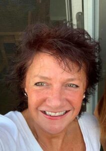 A selfie of Heather smiling at the camera. Heather has short brown hair and is wearing a white top and small hooped earrings.