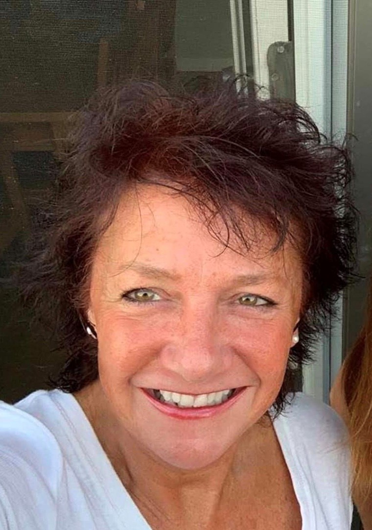 A seflie of Heather Barnfield. Heather has short brown hair and is smiling at the camera. She is wearing earrings and a white t-shirt.