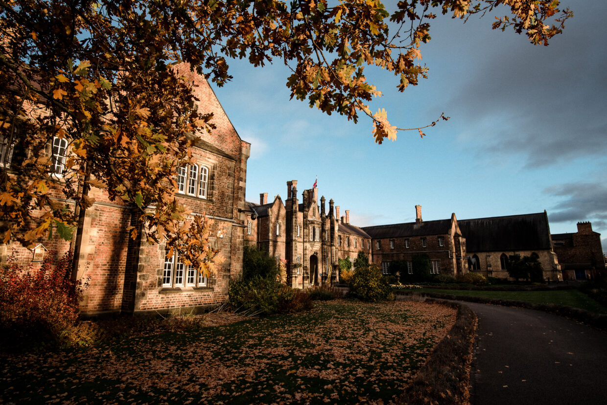 The front of the Lord Mayors Walk campus with the far side in shadow and the near side with autumn sunlight and autumn leaves on the ground.