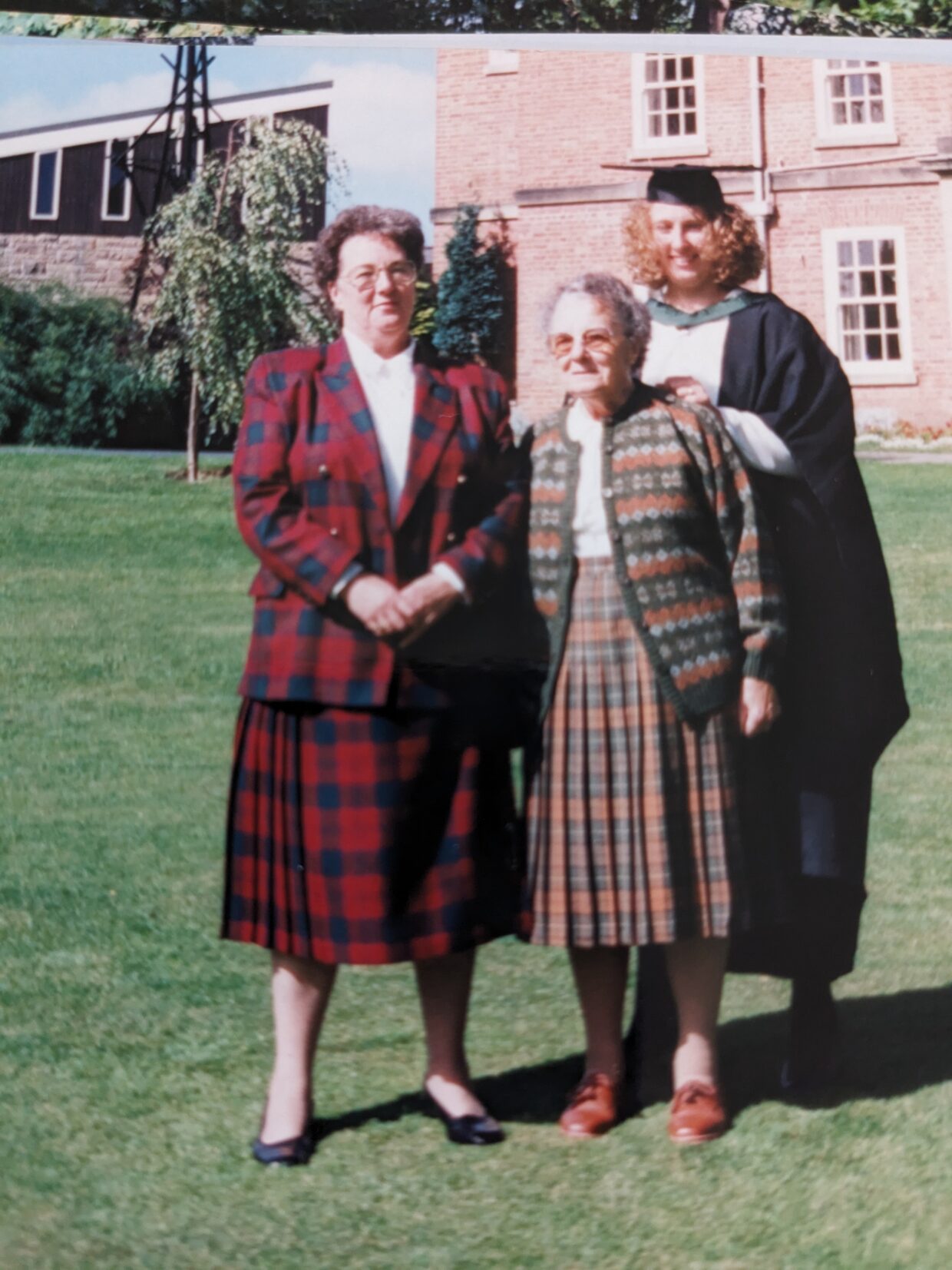 Helen is stood outside Ripon College in a graduation cap and gown. Helen is stood with her mother and grandmother, both wearing tartan skirt suits.