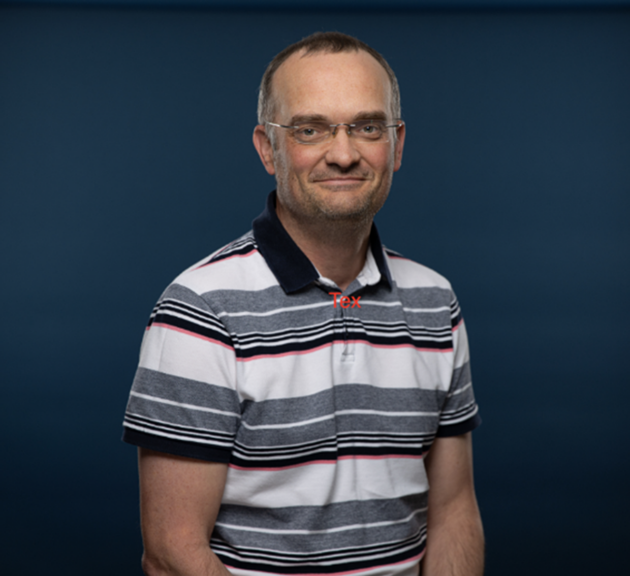 A professional photo of Neil. Neil has short hair and glasses. Neil is wearing a black, white and grey stripped polo shirt