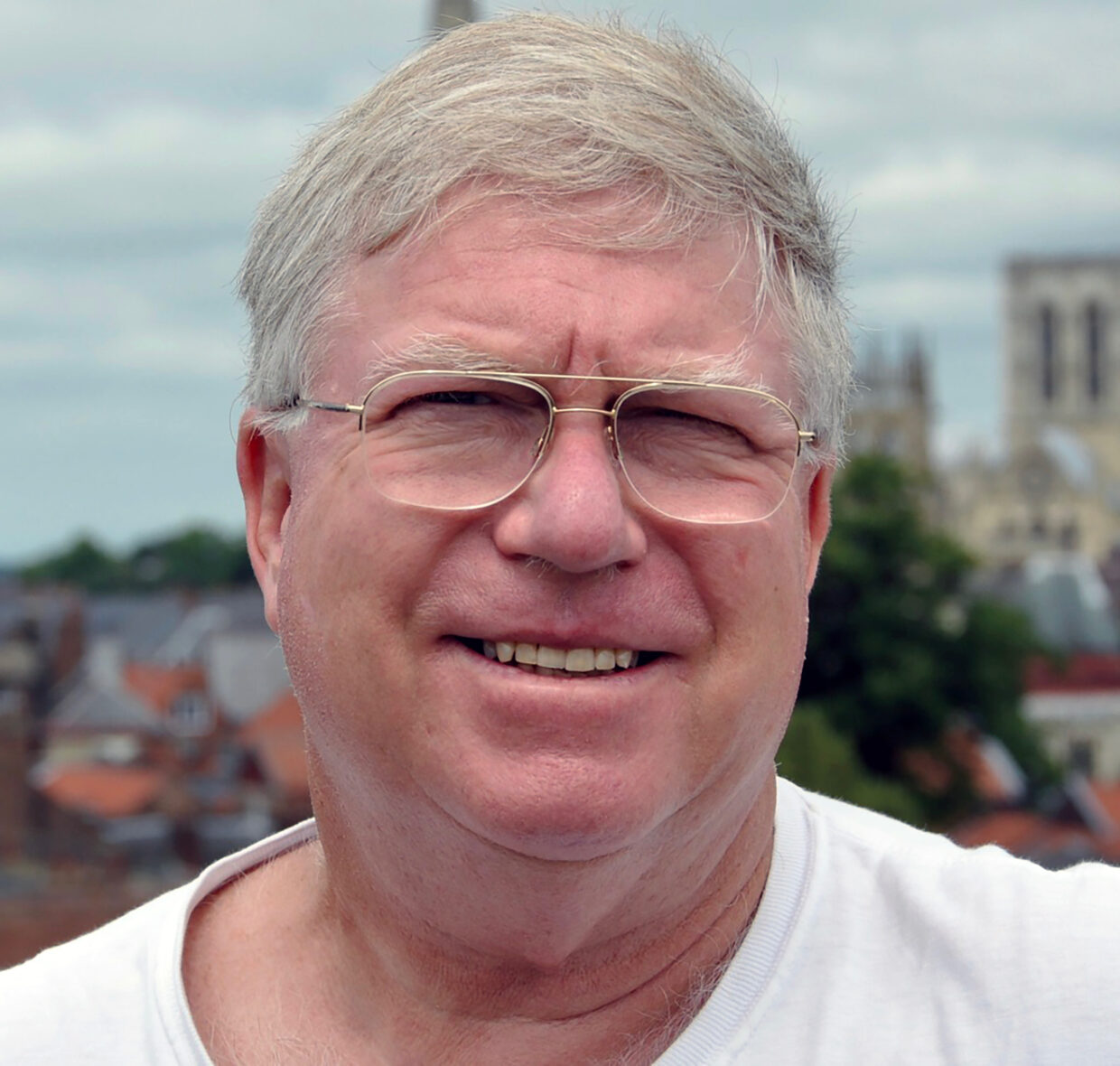 Bill has short white hair and is wearing glasses. Headshot with York Minster in the background.