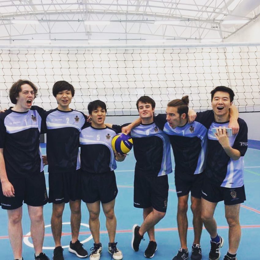 Picture of YSJ volleyball team. 6 people in the picture. Mitchell is on the far left wearing a navy YSJ sports top and shorts and has medium length brown hair.