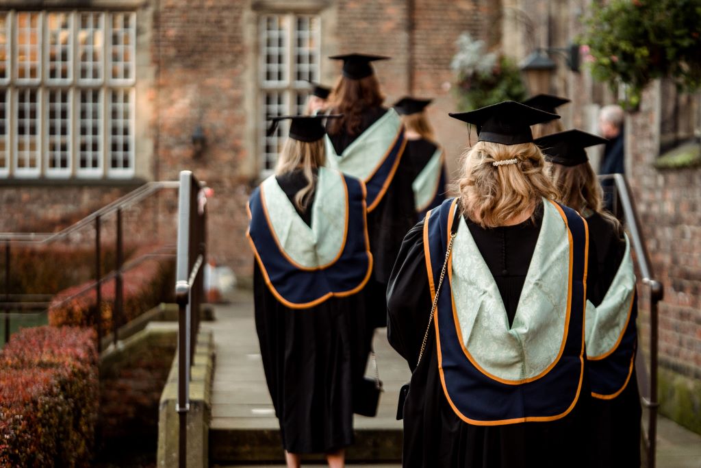 A group of students in graduation gowns walking towards a brick building.