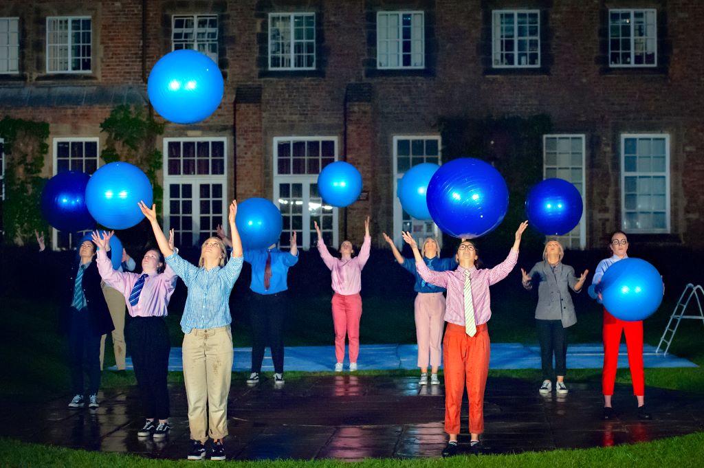 Performing arts students throwing large blue exercise balls into the air.