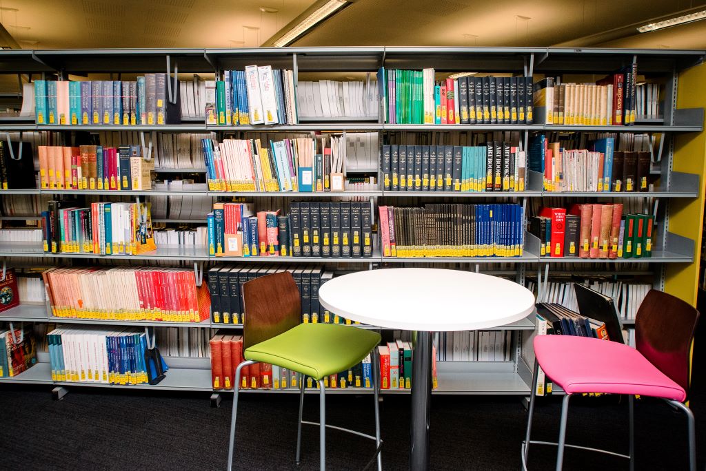 A table with two chairs in front of well-stocked library shelves.