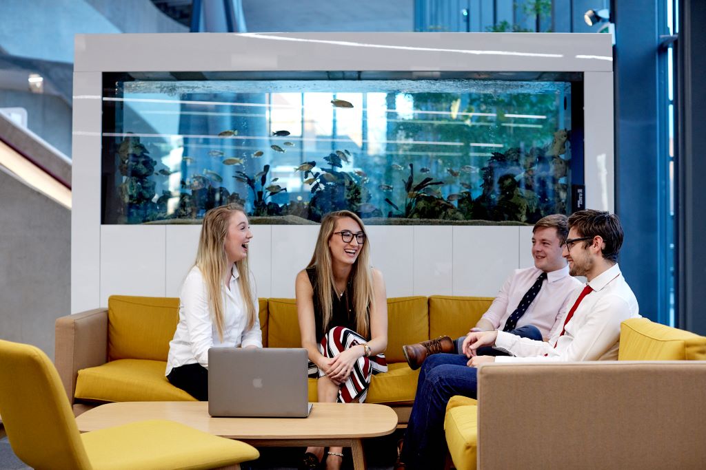 Four students sitting on sofas in front of a fish tank in the Business School.