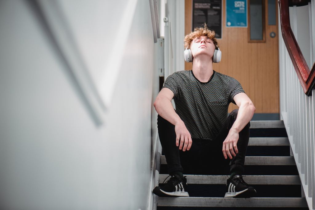A drama student with headphones on, sitting on some stairs looking up