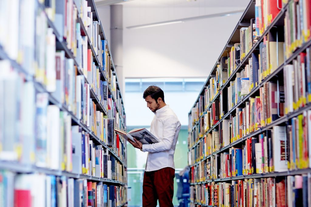 A student or researcher looking at a book in an aisle in Fountains library.