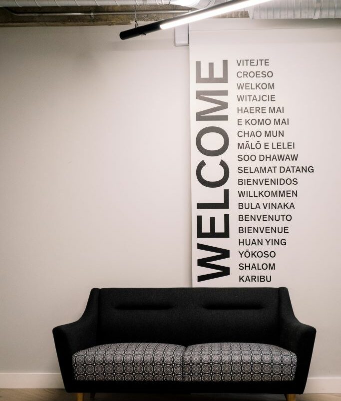 A sofa with the word 'Welcome' written on the wall behind in different languages.