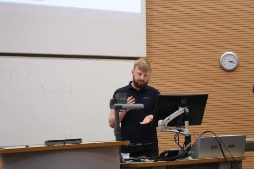 Photograph of student stood behind a computer at the front of a lecture theater presenting.
