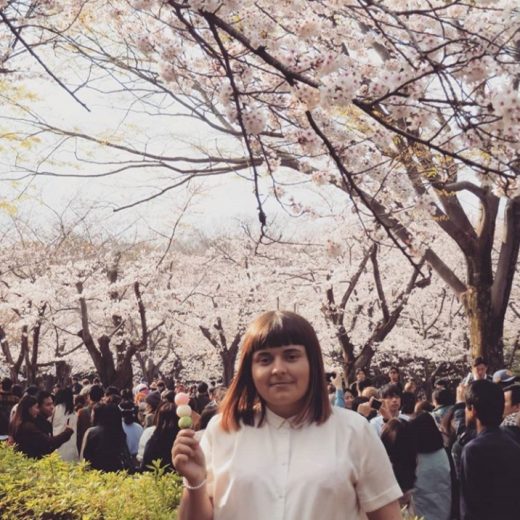 Image of student holding an icecream in front of blush pink blossom trees