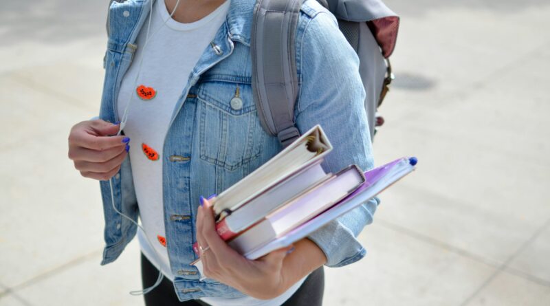 Image of someone holding books, a backpack and headphones